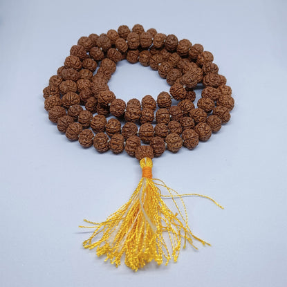 A strand of brown textured prayer beads with a yellow tassel, arranged in a circle on a light gray background.